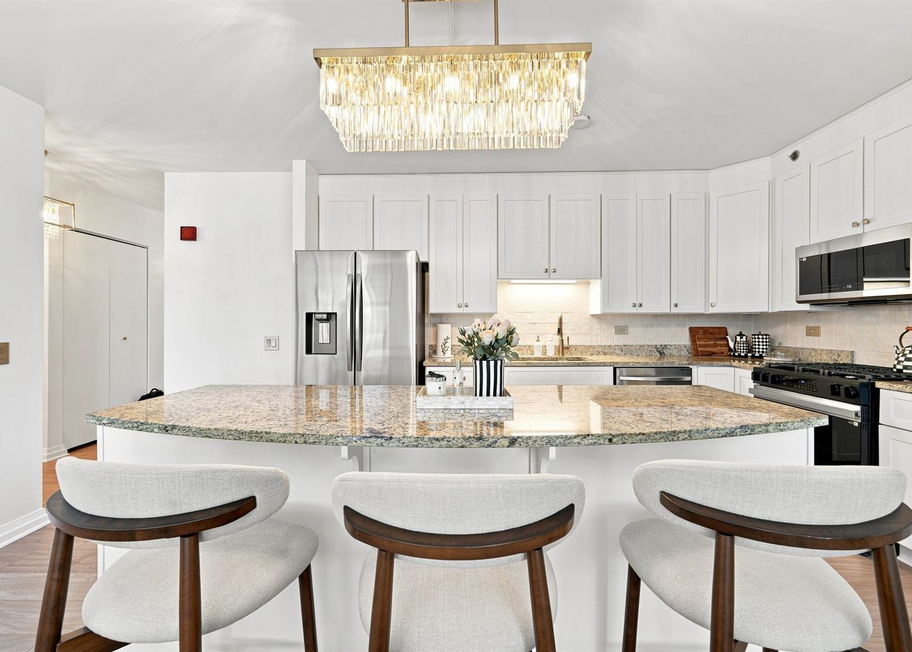 The same kitchen after renovation: white shaker cabinetry, brass linear pendant, new island and white oak floors