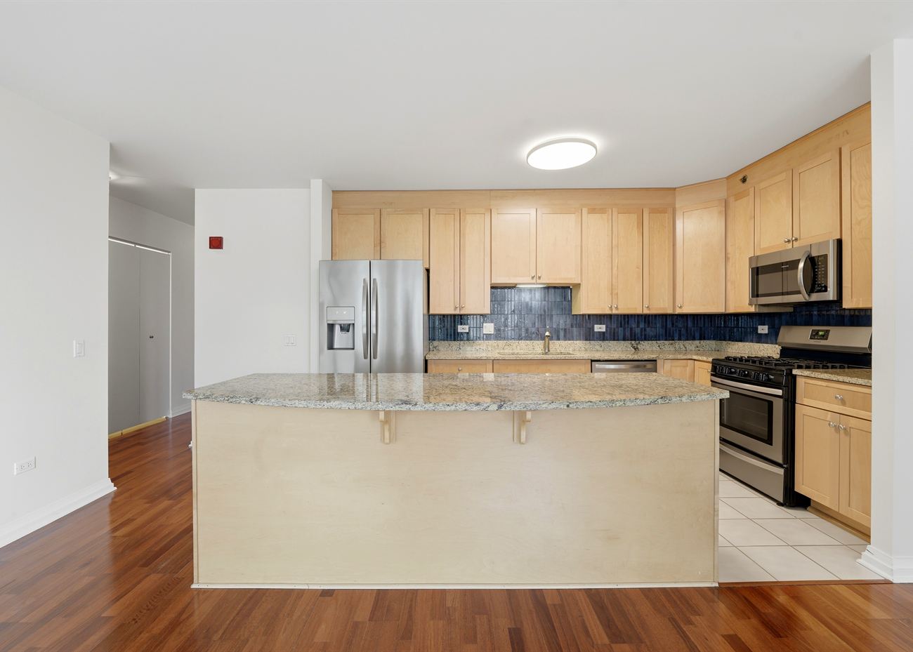 The kitchen at 33 W Ontario before renovation: maple cabinetry, blue tile backsplash, granite island and tiled floor