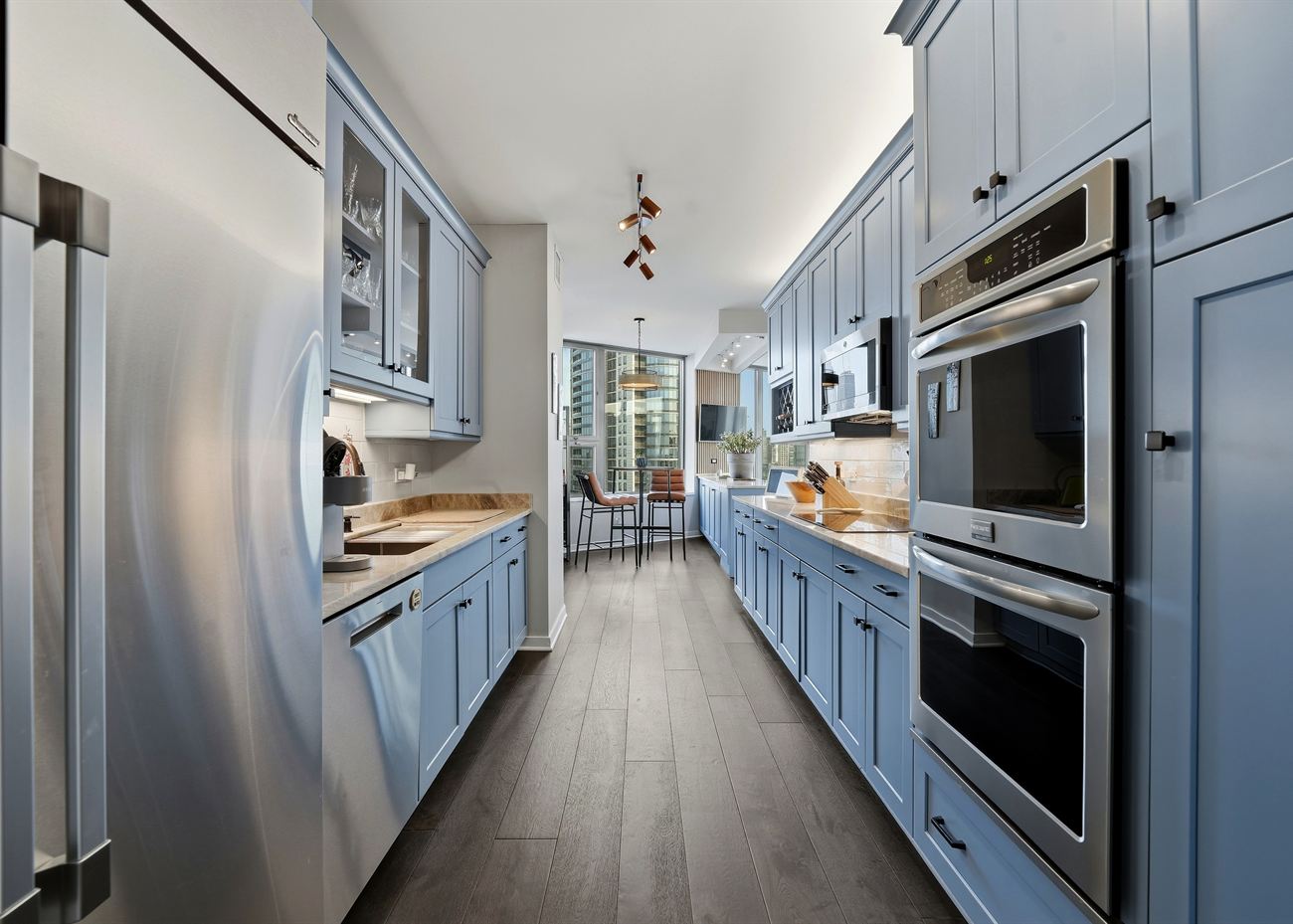 The same galley kitchen after renovation: powder-blue shaker cabinetry, pale stone counters and a dark wood floor
