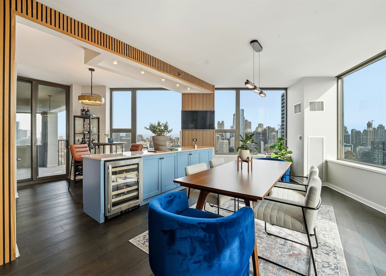 The same room after renovation: white-oak slat wall, powder-blue cabinetry, walnut dining table and sculptural pendant