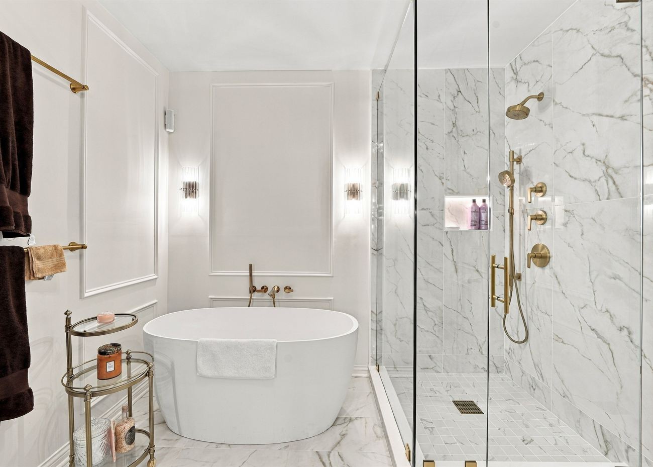 The same bathroom after renovation: freestanding tub, marble walls and brass fittings