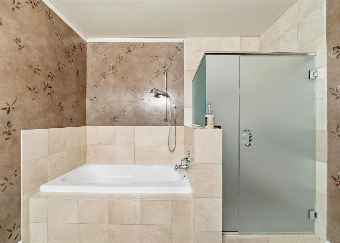 The primary bathroom before renovation: decked-in jetted tub, beige tile and a frosted glass enclosure