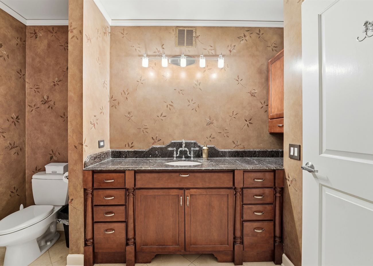 The vanity before renovation: dark timber cabinet, granite top and a bar of exposed bulbs