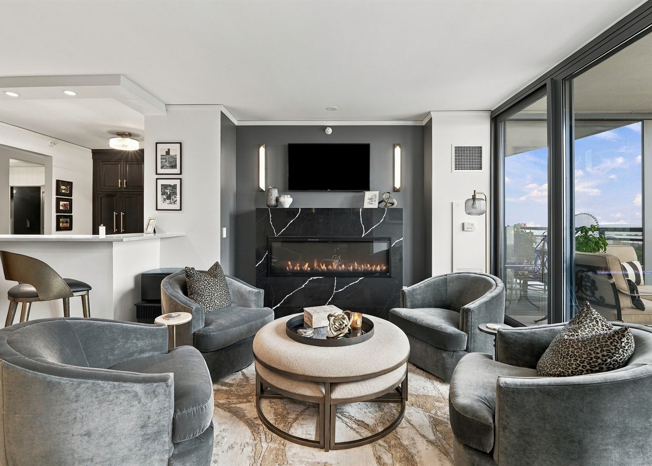 The same living room after renovation: linear fireplace in stone, swivel chairs and an open kitchen beyond