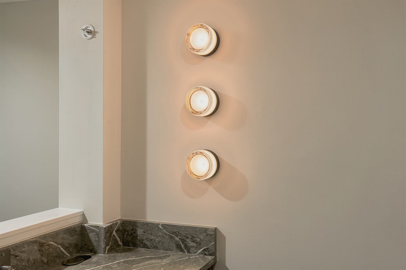 Three stacked wall sconces above a green marble return